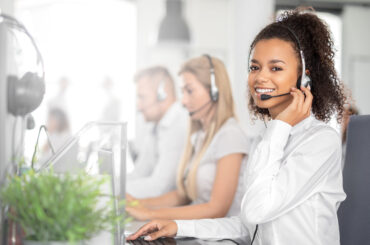 Call center worker accompanied by her team. Smiling customer support operator at work. Young employee working with a headset.