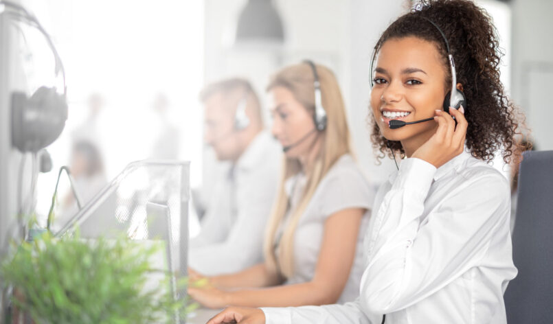 Call center worker accompanied by her team. Smiling customer support operator at work. Young employee working with a headset.